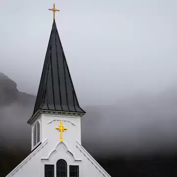 White wooden steeple with a yellow cross and dark spire at Grytviken, South Georgia, set against fog-shrouded mountains