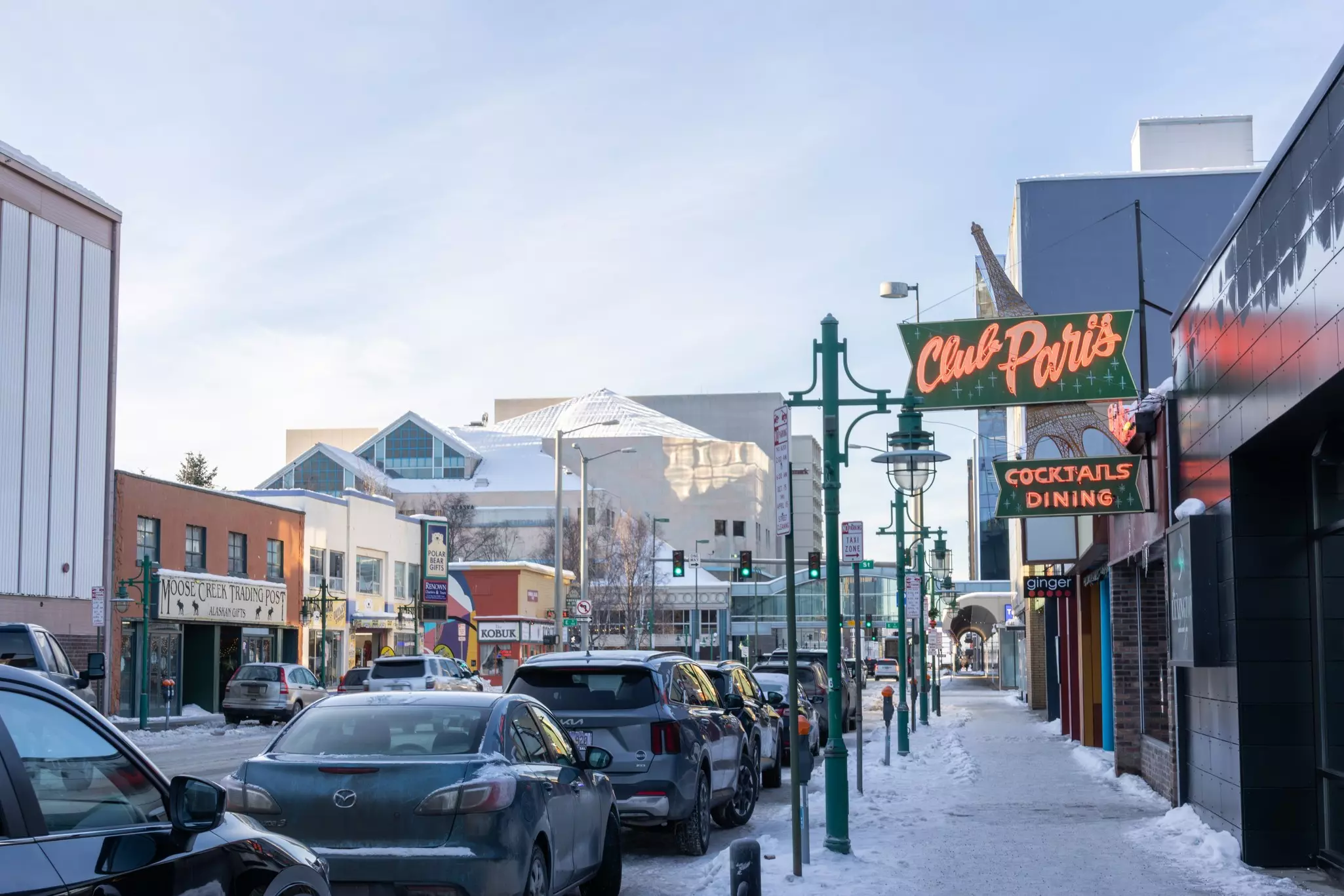 Shops in a downtown area; one has a neon sign for Club Paris. 