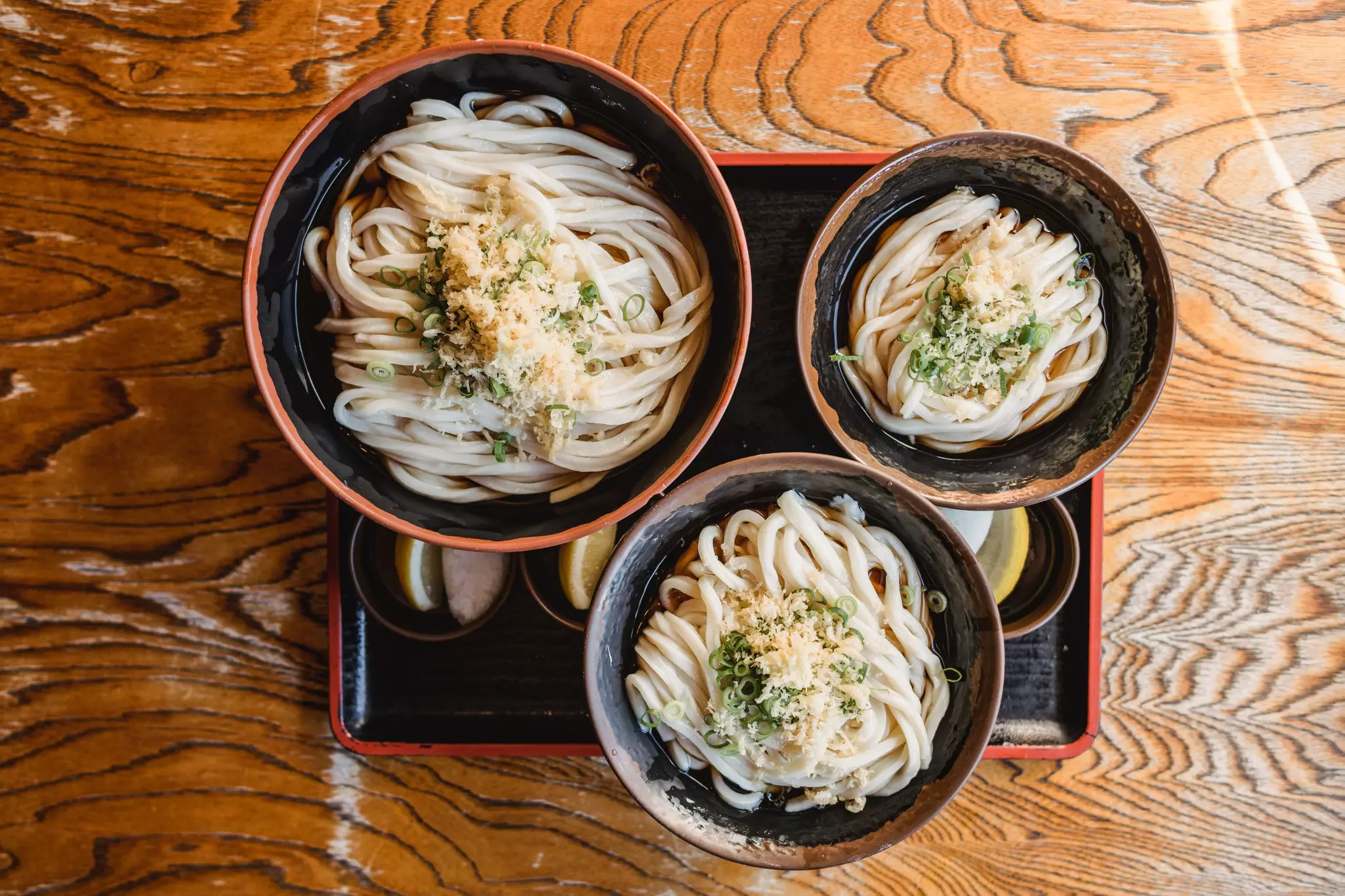 The three different sized bowls of udon on a small tray on a wooden table