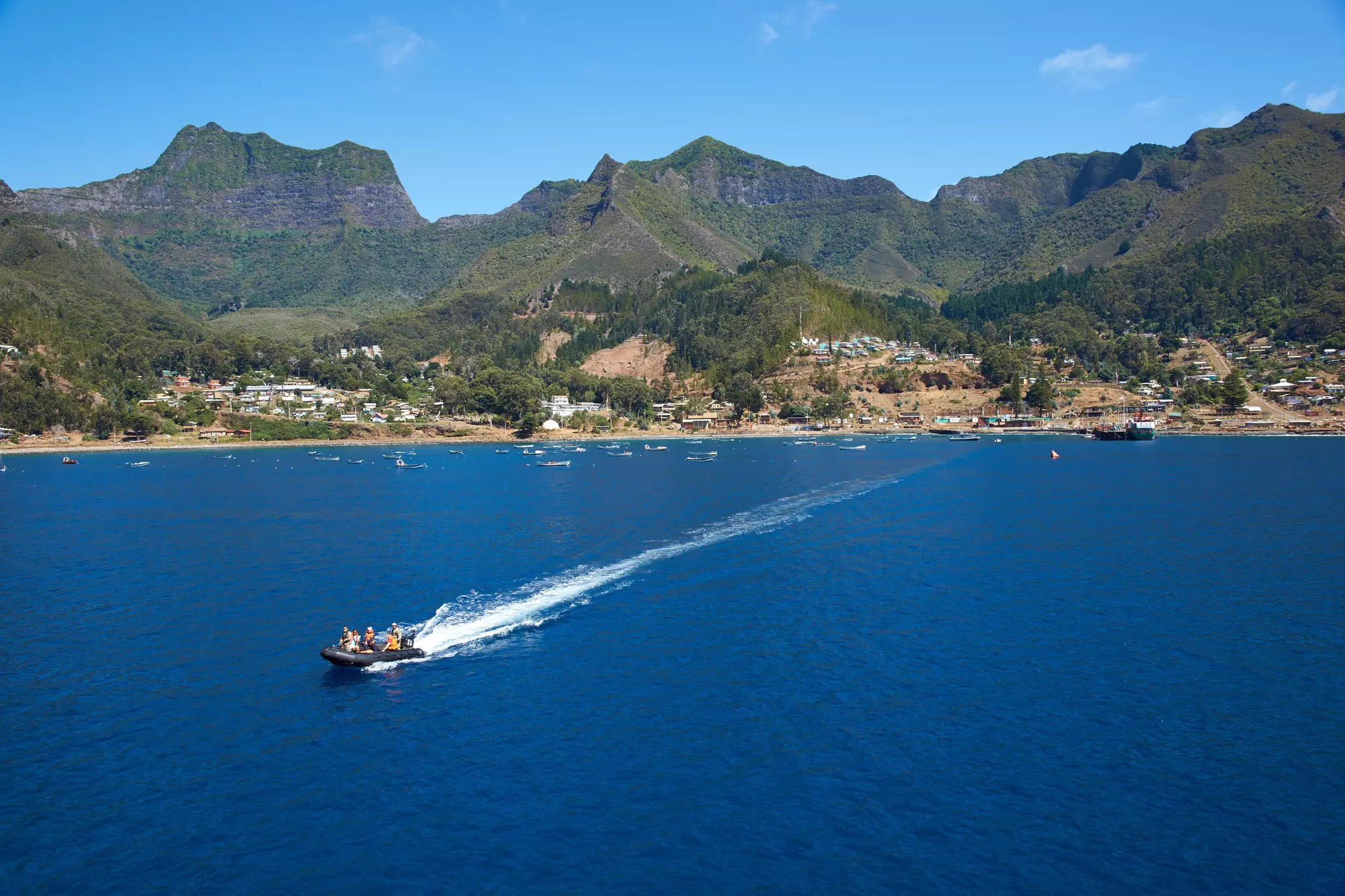 People on a RIB zip across a bay in front of a small-town settlement on an island