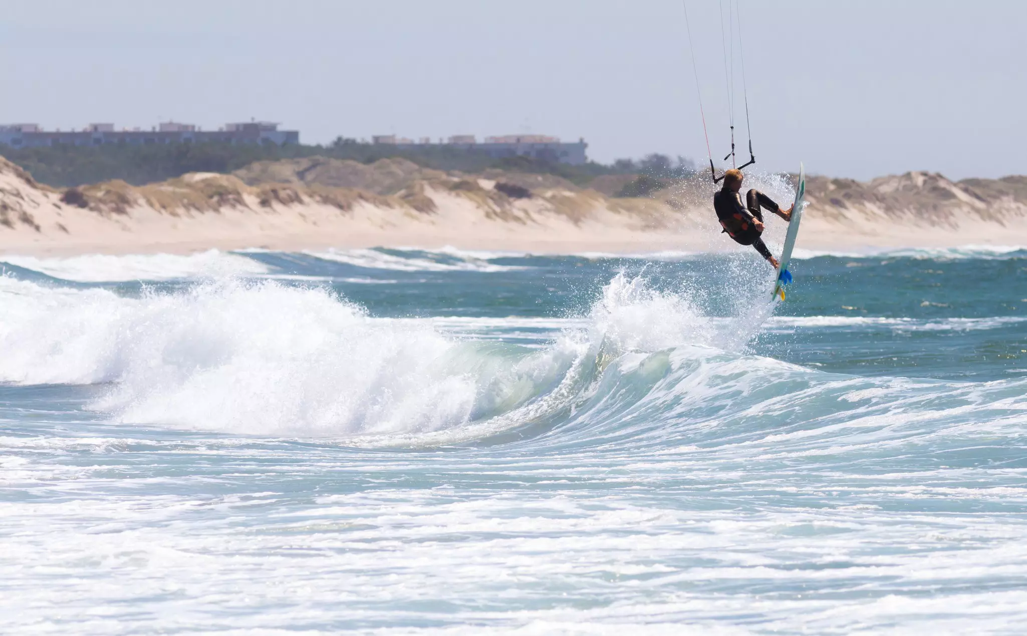 A kitesurfer jumps from a wave at Cabedelo Beach, Viana do Castelo, Portugal, with dunes behind.