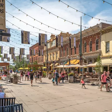 People walking on pedestrian streets lined with restaurants and shops on a sunny day.