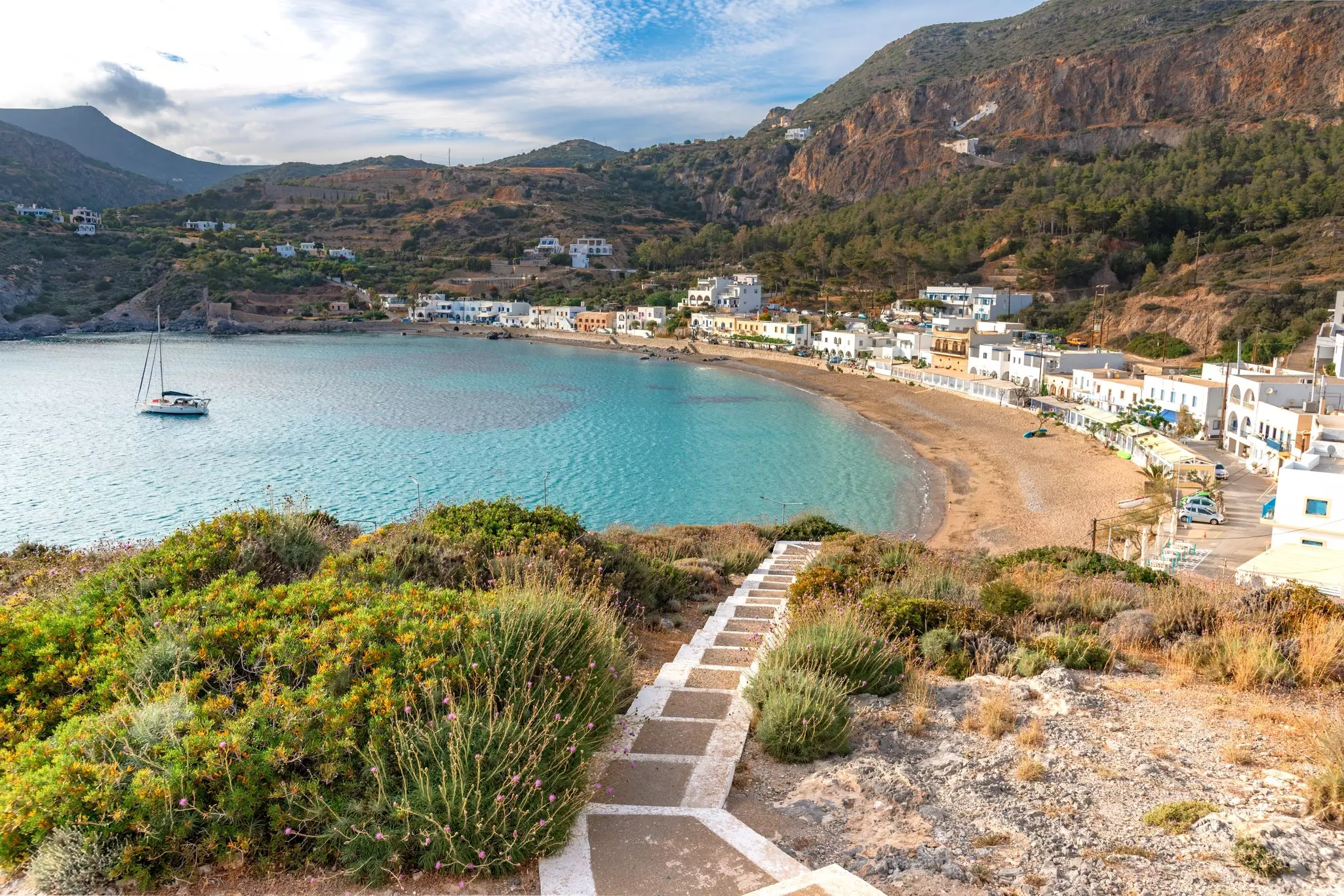 A path on a hill leads toward a cove and beachfront village.