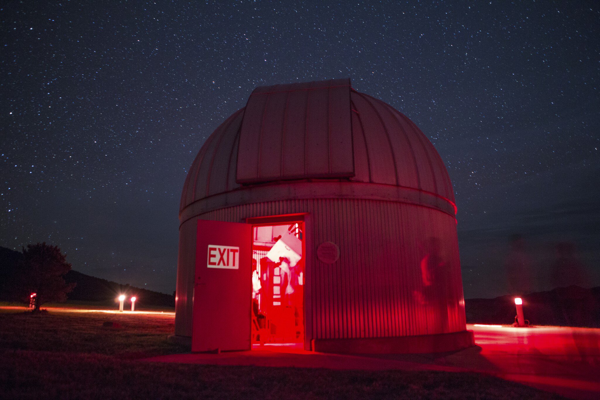 A telescope dome lit red at night, its shutter open to a star-filled sky.