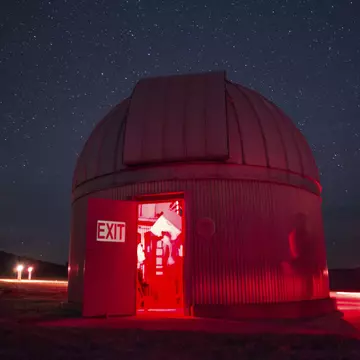 A telescope dome lit red at night, its shutter open to a star-filled sky.