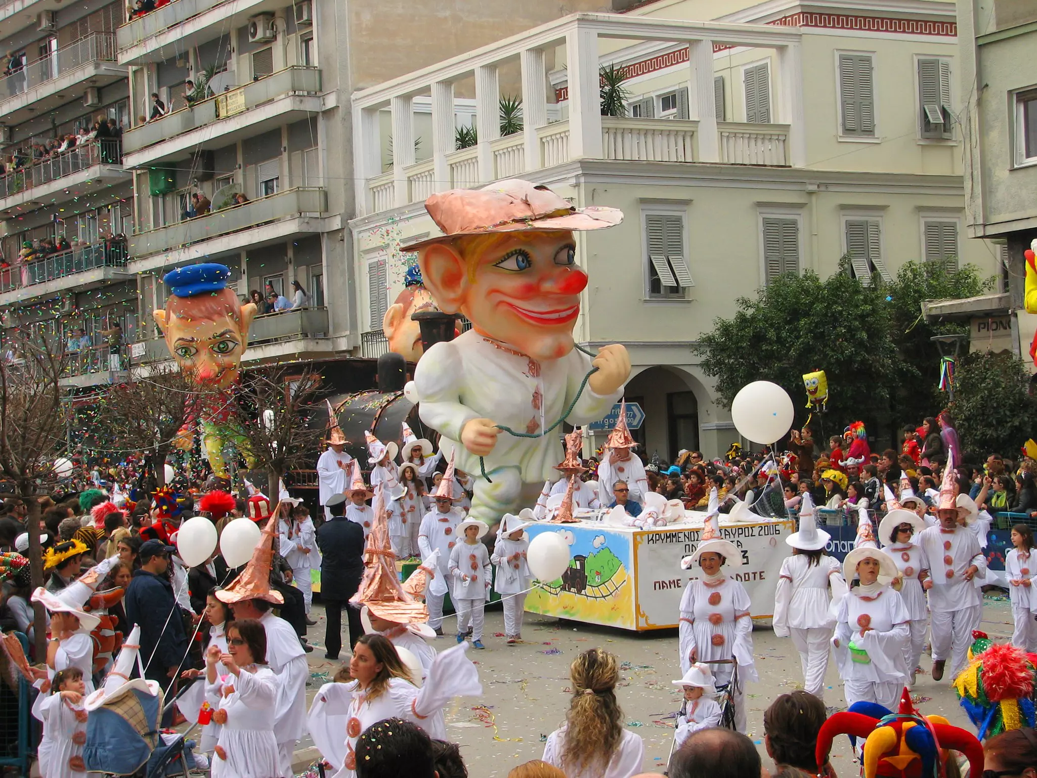People in costume walk alongside a float of a large figure in a parade.