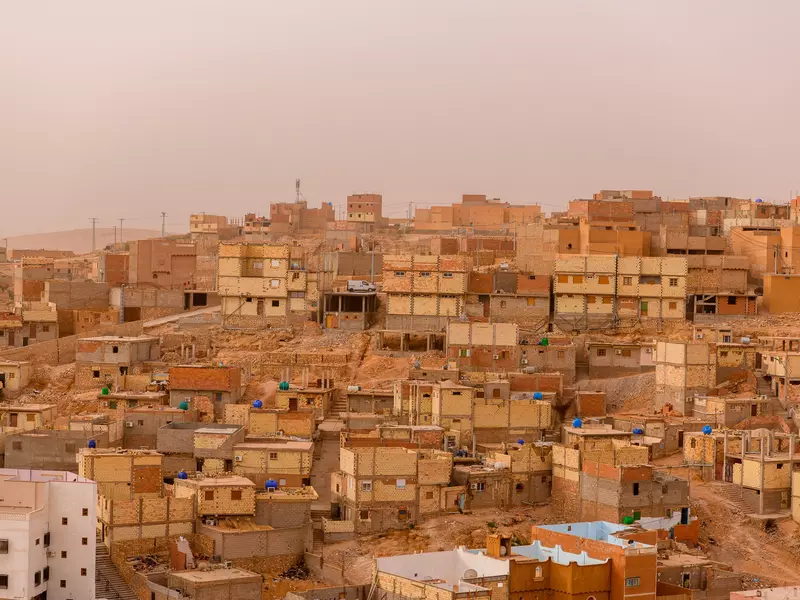 A panoramic view of an ancient city in Algeria, with low golden buildings on a hillside against a dusky sky.