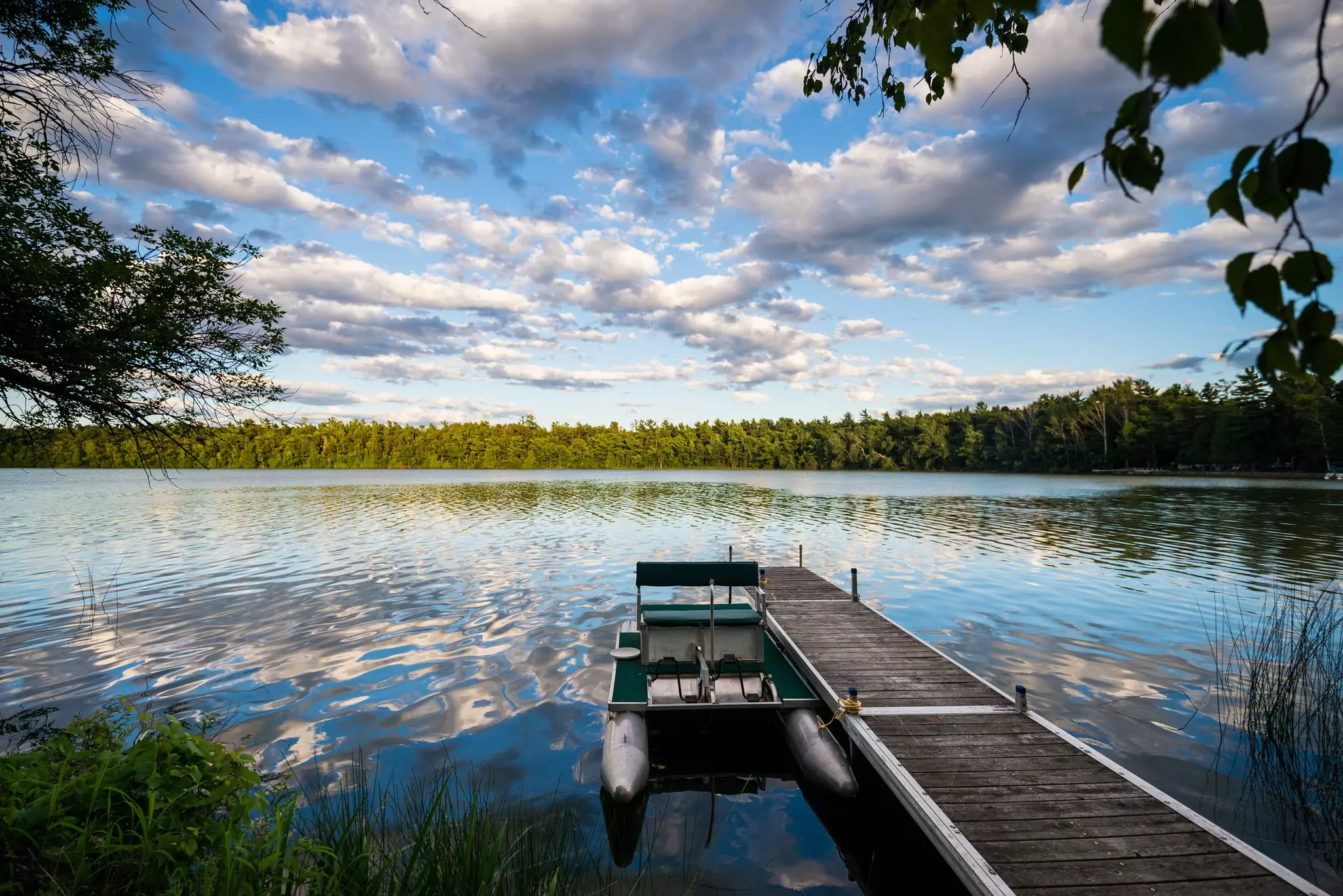 A wooden pier leading out into a lake with a pedal boat moored at the end