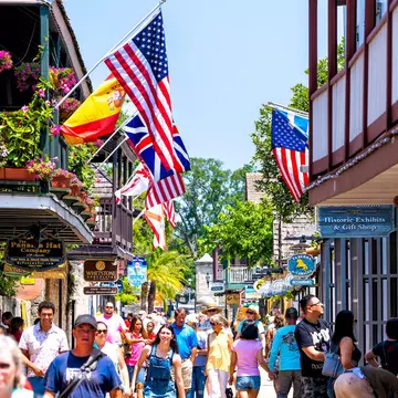 People shopping on St George St by stores, shops and restaurants American and international flags, St Augustine, Florida, USA