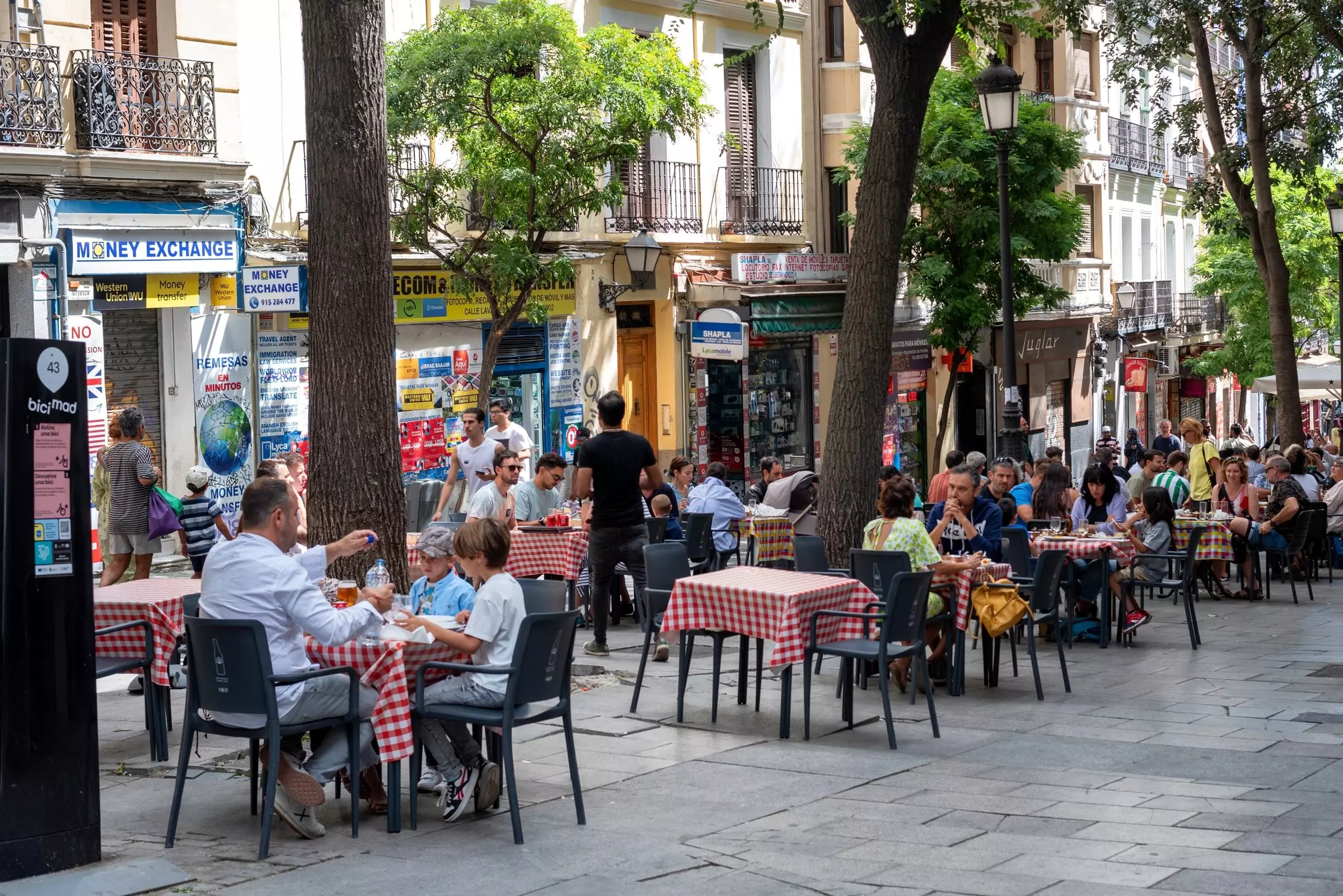People dine at outdoor tables on a street in a city.