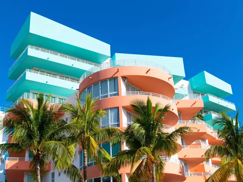 Turquoise and orange art deco building with palm trees in the foreground.
