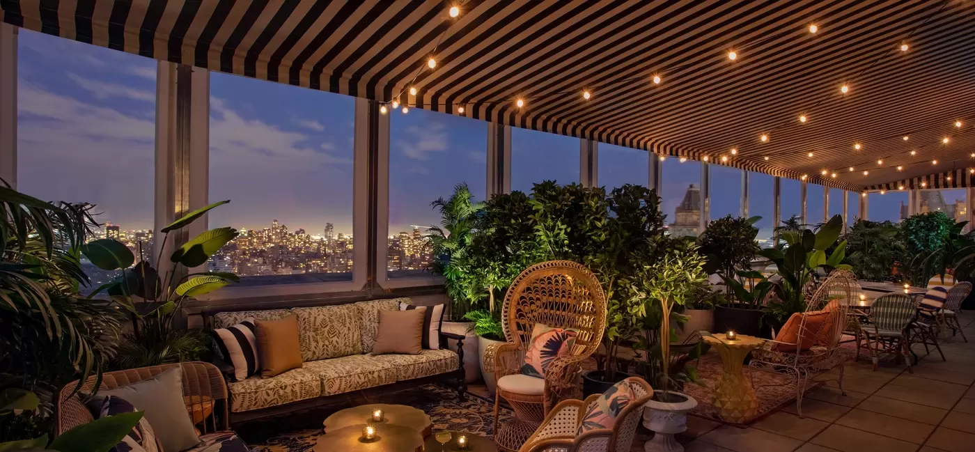 Couches and chairs at a rooftop bar under an awning with white lights strung across.