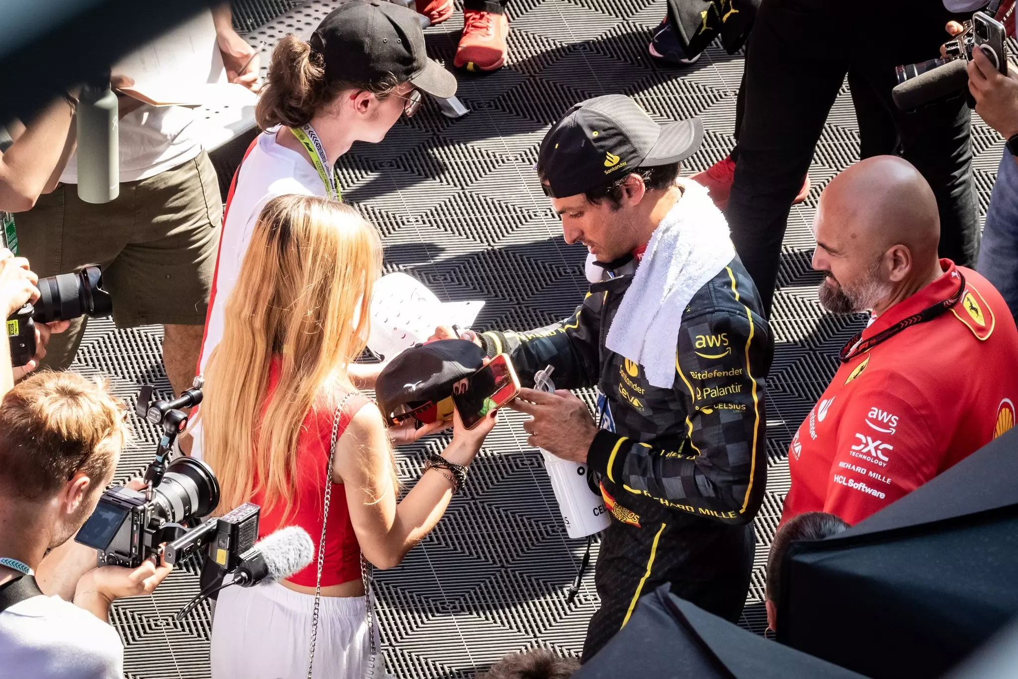 A man in a black racecar driver uniform signs an autograph for a fan