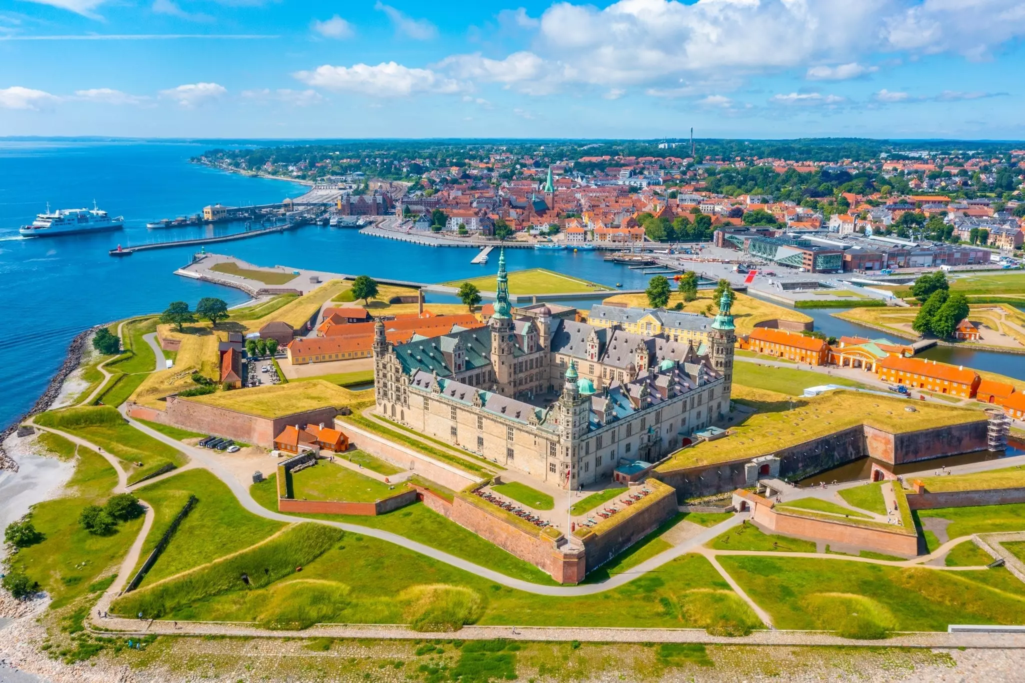 Panorama of a castle with a sea and city in the distance on a sunny day.