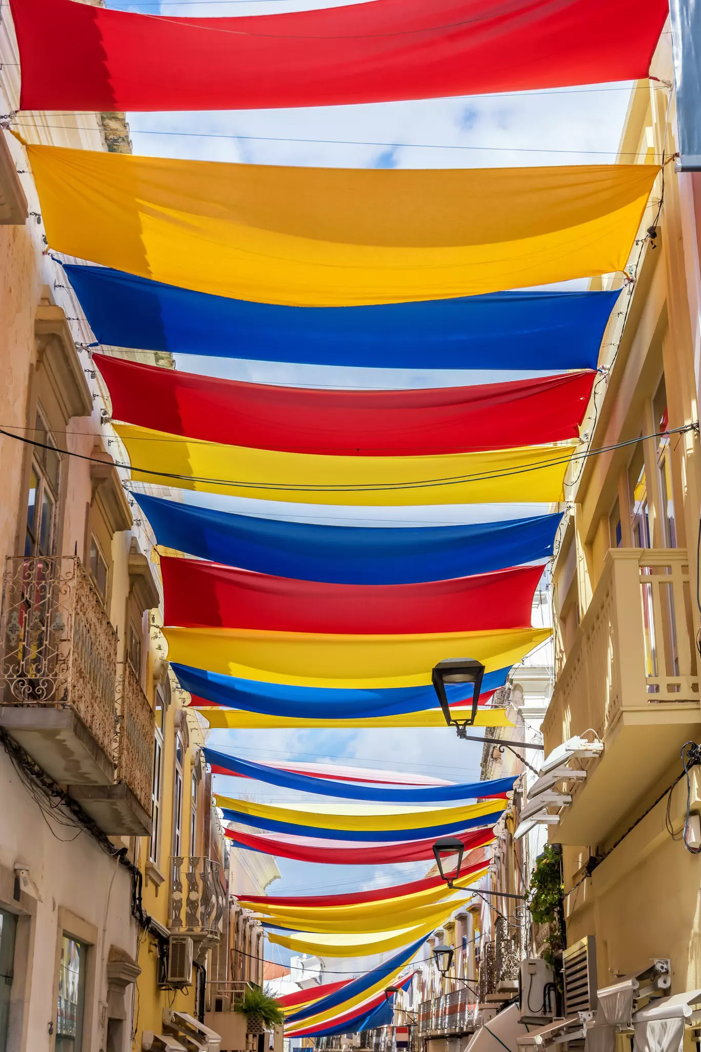 Red, yellow and blue sunshades over a narrow street.