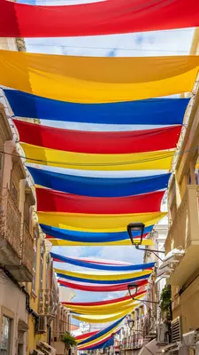 Red, yellow and blue sunshades over a narrow street.
