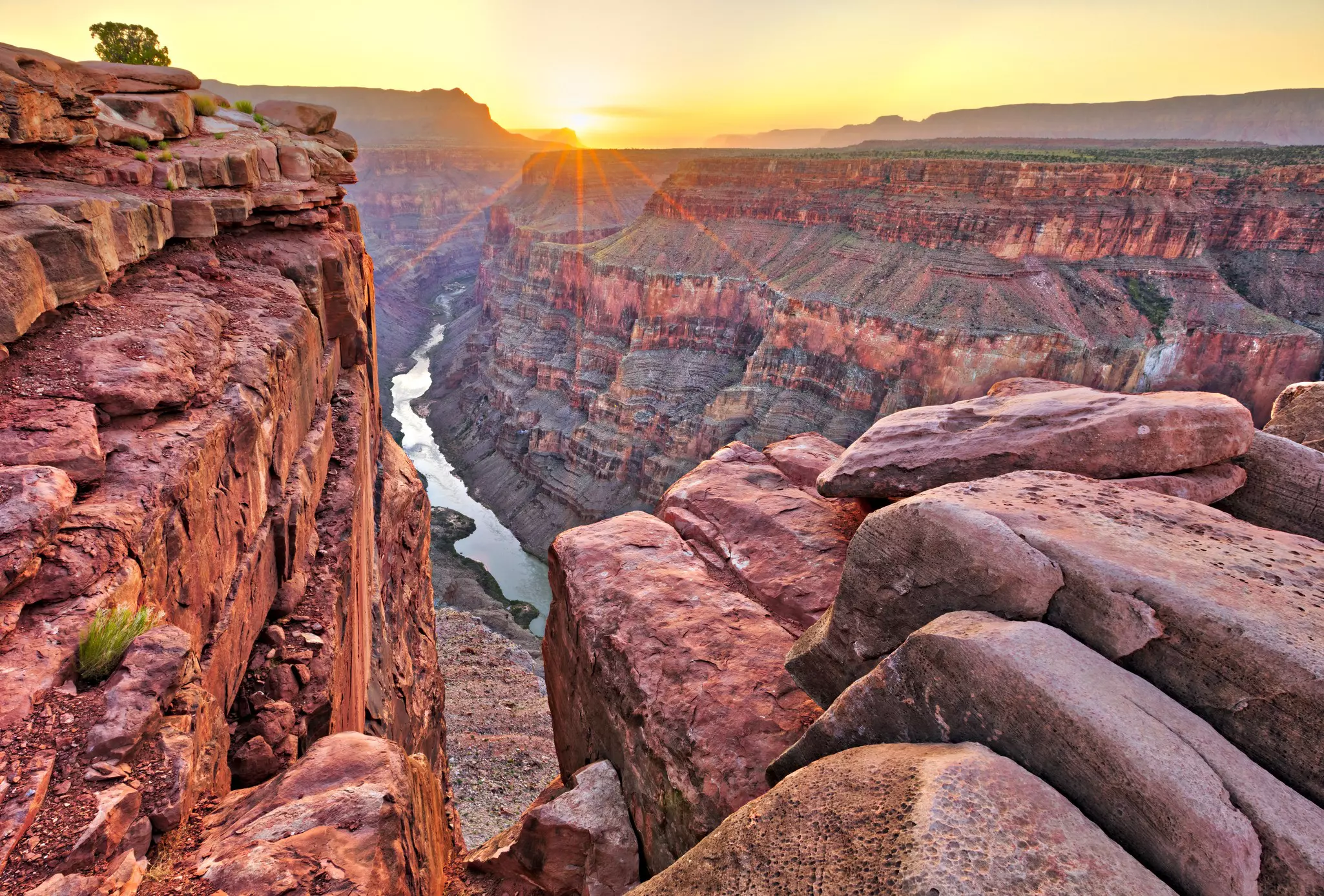Sunrise at a viewpoint above a river that has carved a rocky canyon with many different colors glowing in the rocks in the early morning light.