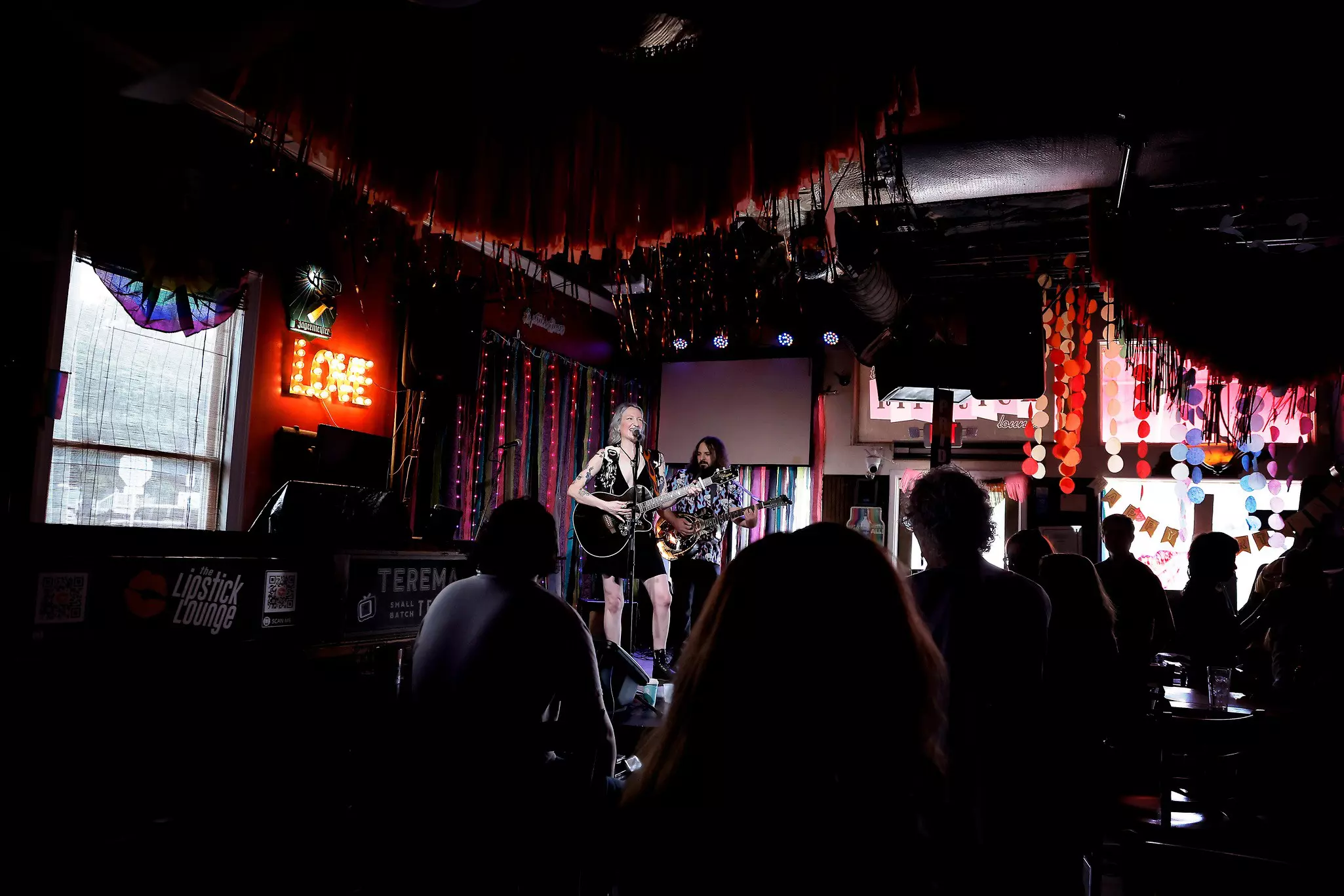 A performer plays the guitar on the small stage of dimly lit bar