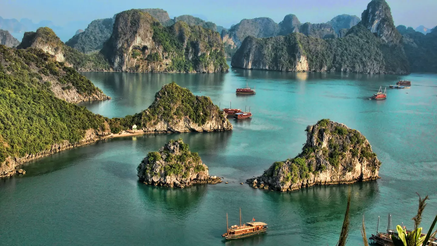 I high vantage point image of a collection of tour boats and cruise ships passing by limestone islands in Halong Bay