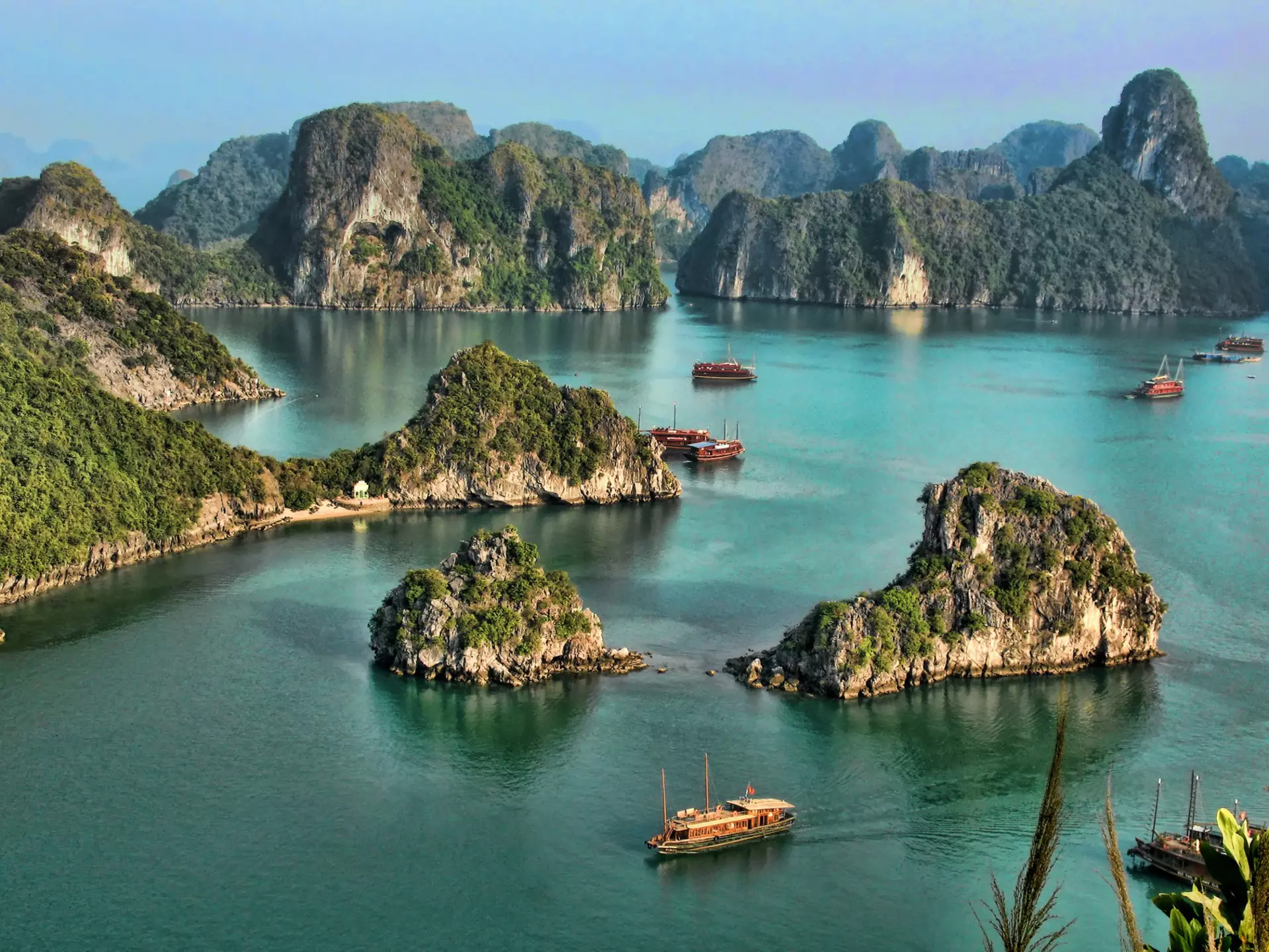 I high vantage point image of a collection of tour boats and cruise ships passing by limestone islands in Halong Bay
