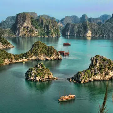 I high vantage point image of a collection of tour boats and cruise ships passing by limestone islands in Halong Bay