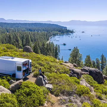 Aerial shot of a campervan at a viewpoint with two people sat overlooking a lake