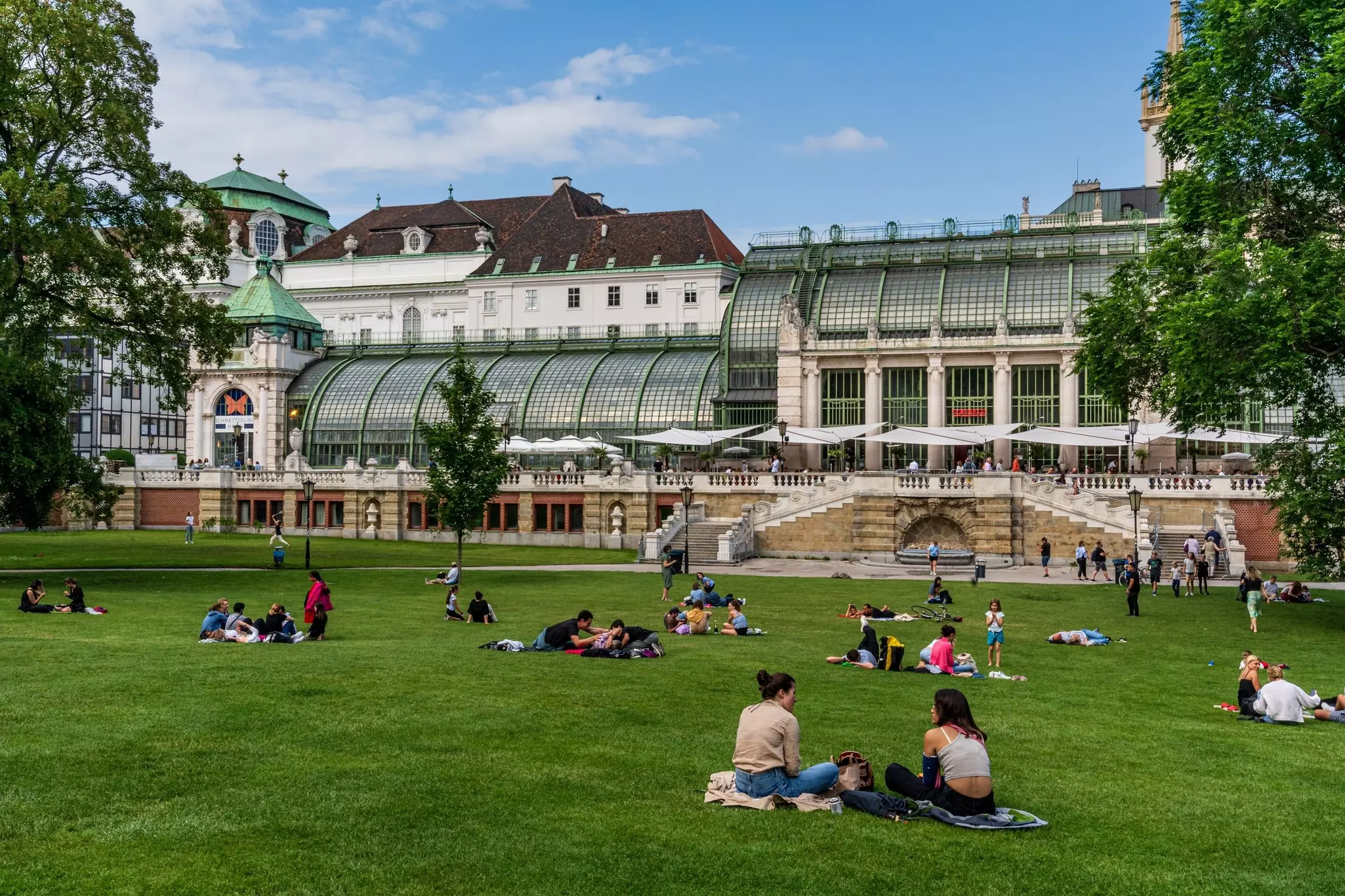 Visitors relaxing in the Burggarten, a statue-filled palace garden with an art nouveau conservatory