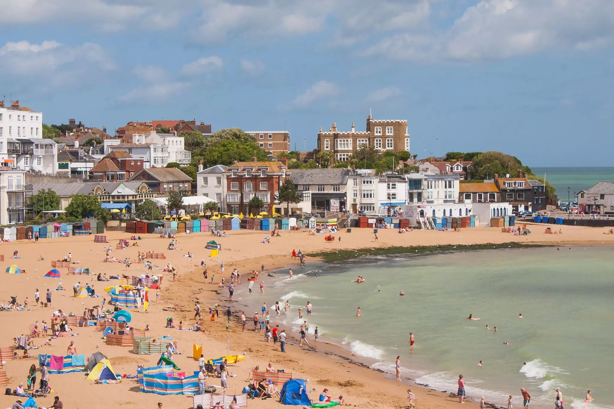 Swimmers and sunbathers on a sandy town beach on a summer's day.