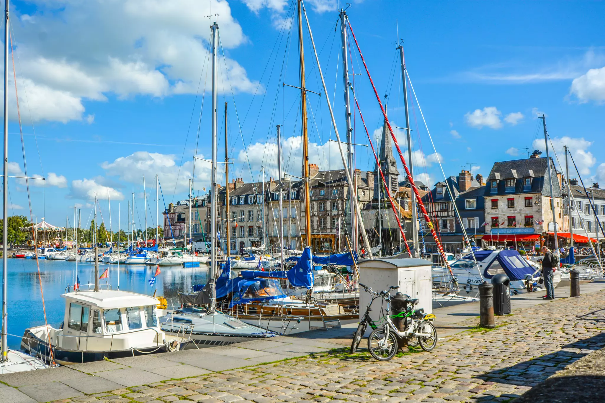 Two bicycles parked along a cobblestone road as boats line the harbor on the Normandy coast of France in the Old Pier at Honfleur, France