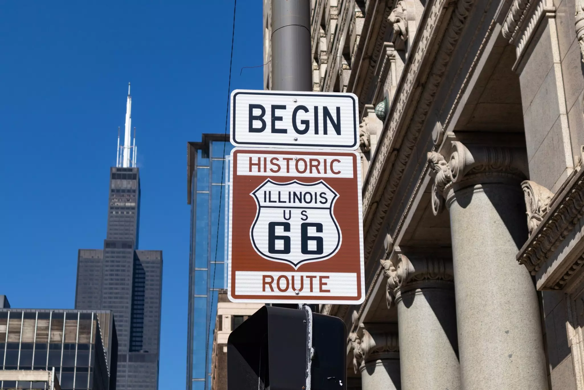 A brown and white street sign marking the start of a driving route for Route 66.
