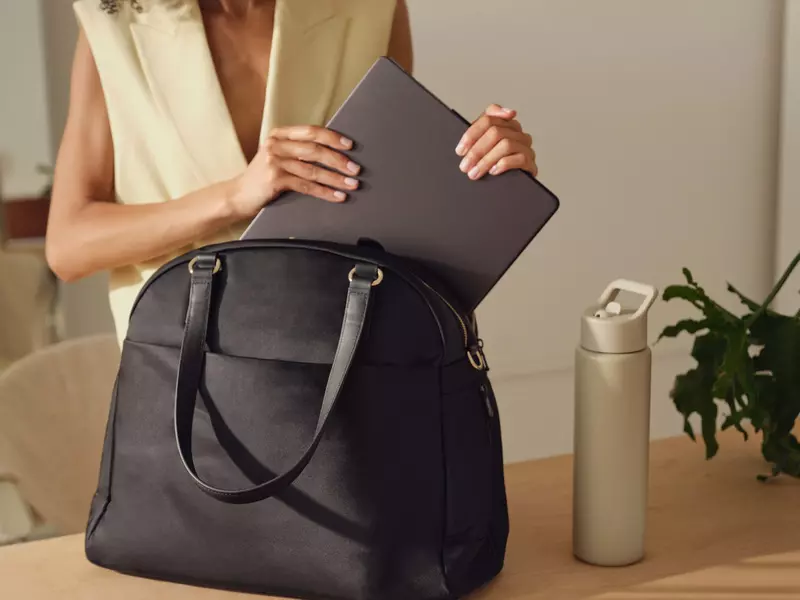 A person putting a silver laptop in a black bag with handles.