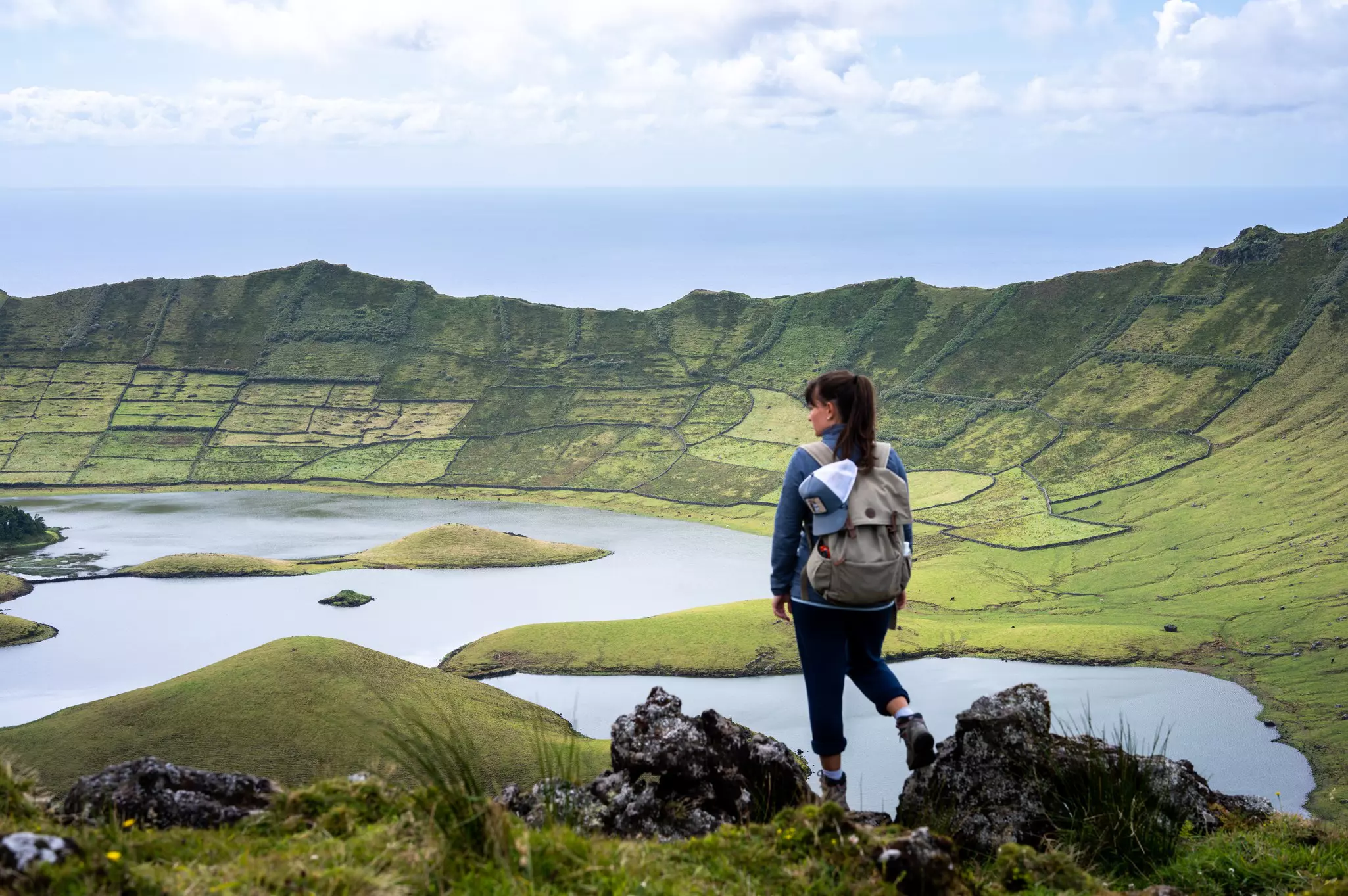 Aerial view of lush green caldera at on an overcast day with a female hiker overlooking the scene