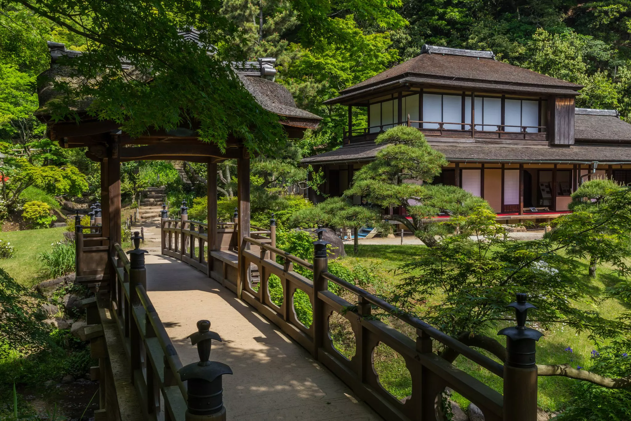 Japanese-style architecture building and bridge surrounded by greenery on a sunny day.