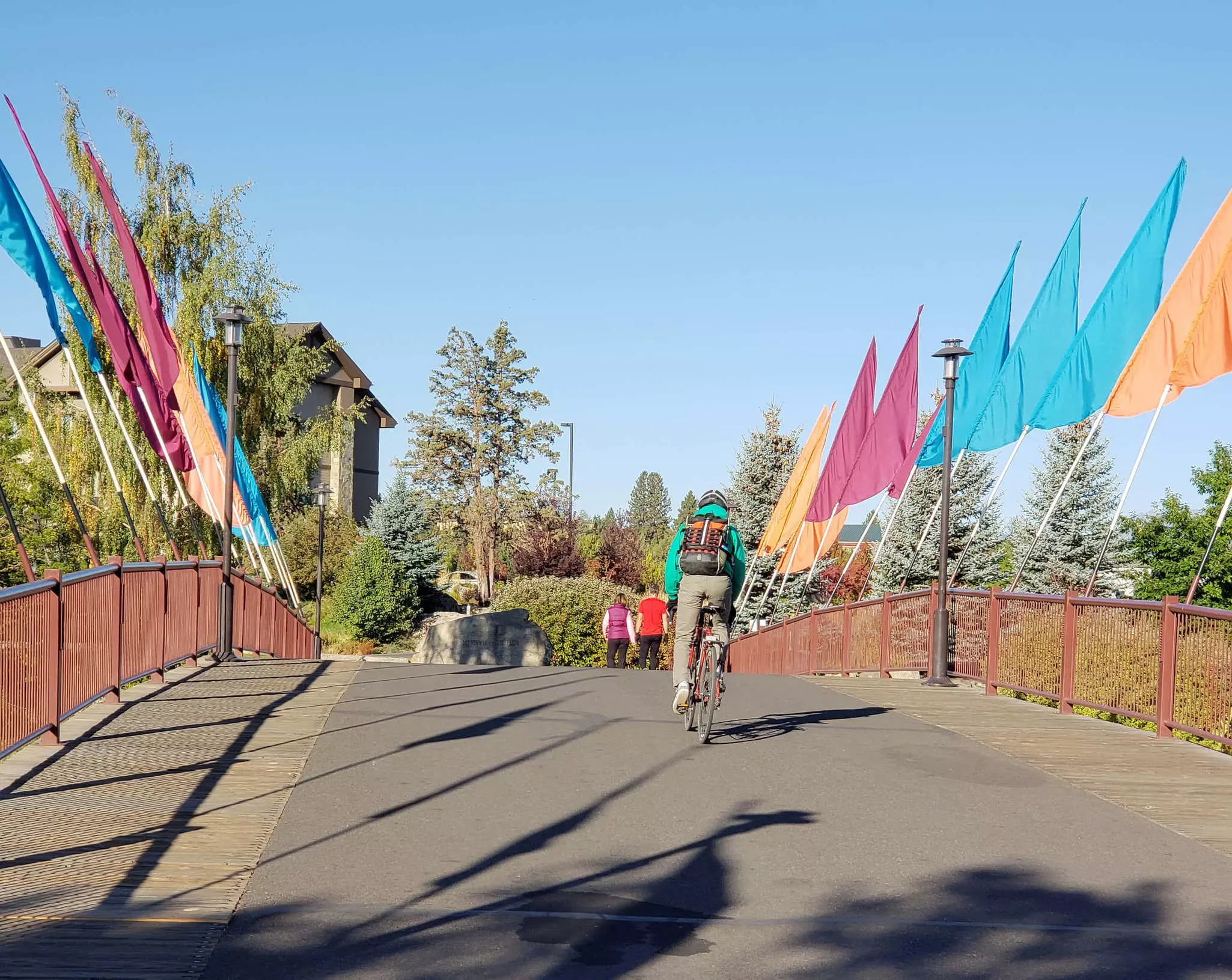 A bicyclist rides across a bridge with multi-colored flags that crosses the Deschutes River at the Old Mill District in Bend in Central Oregon