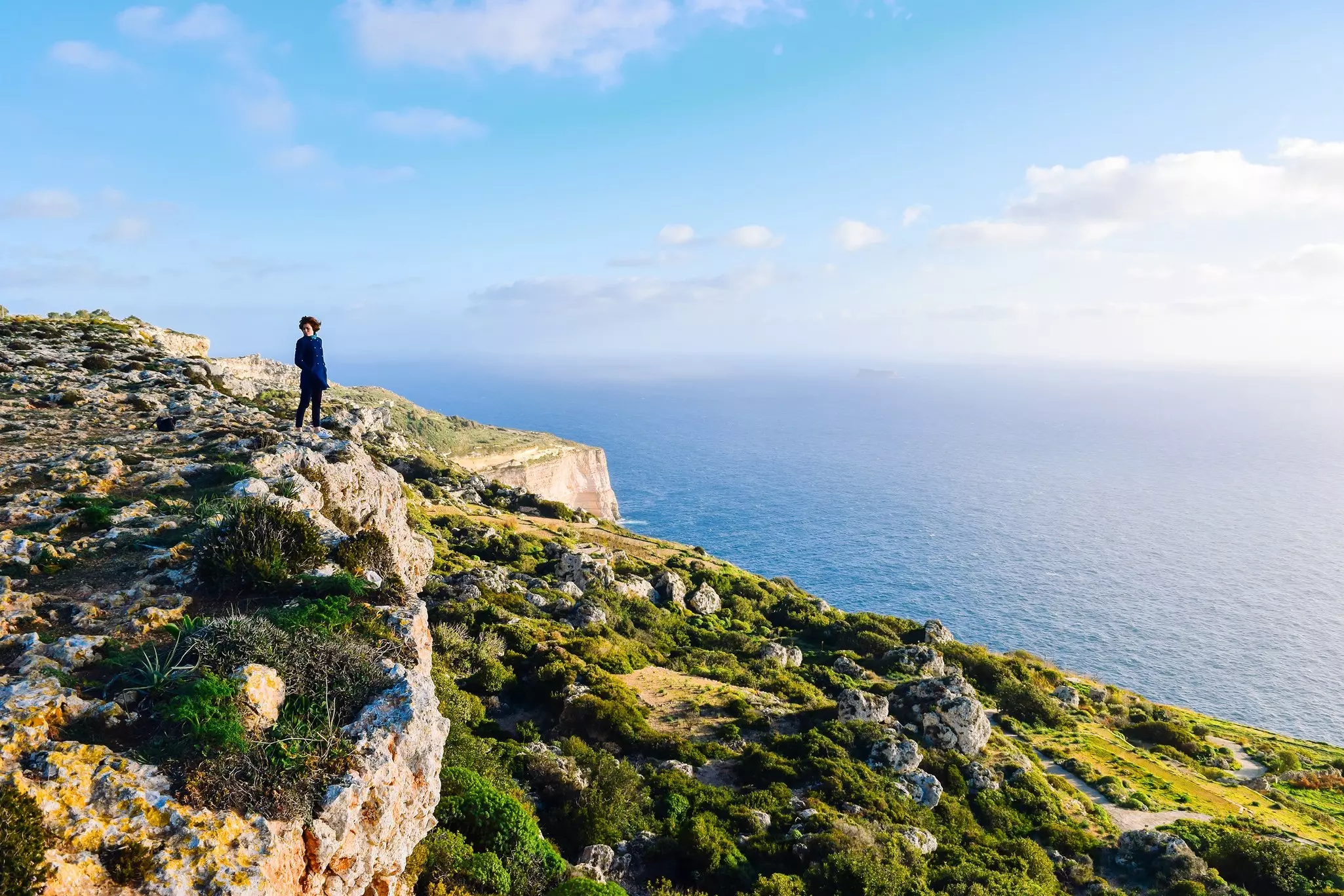 A hiker on a green slope of the Dingli Cliffs overlooking the blue Mediterranean Sea, Malta
