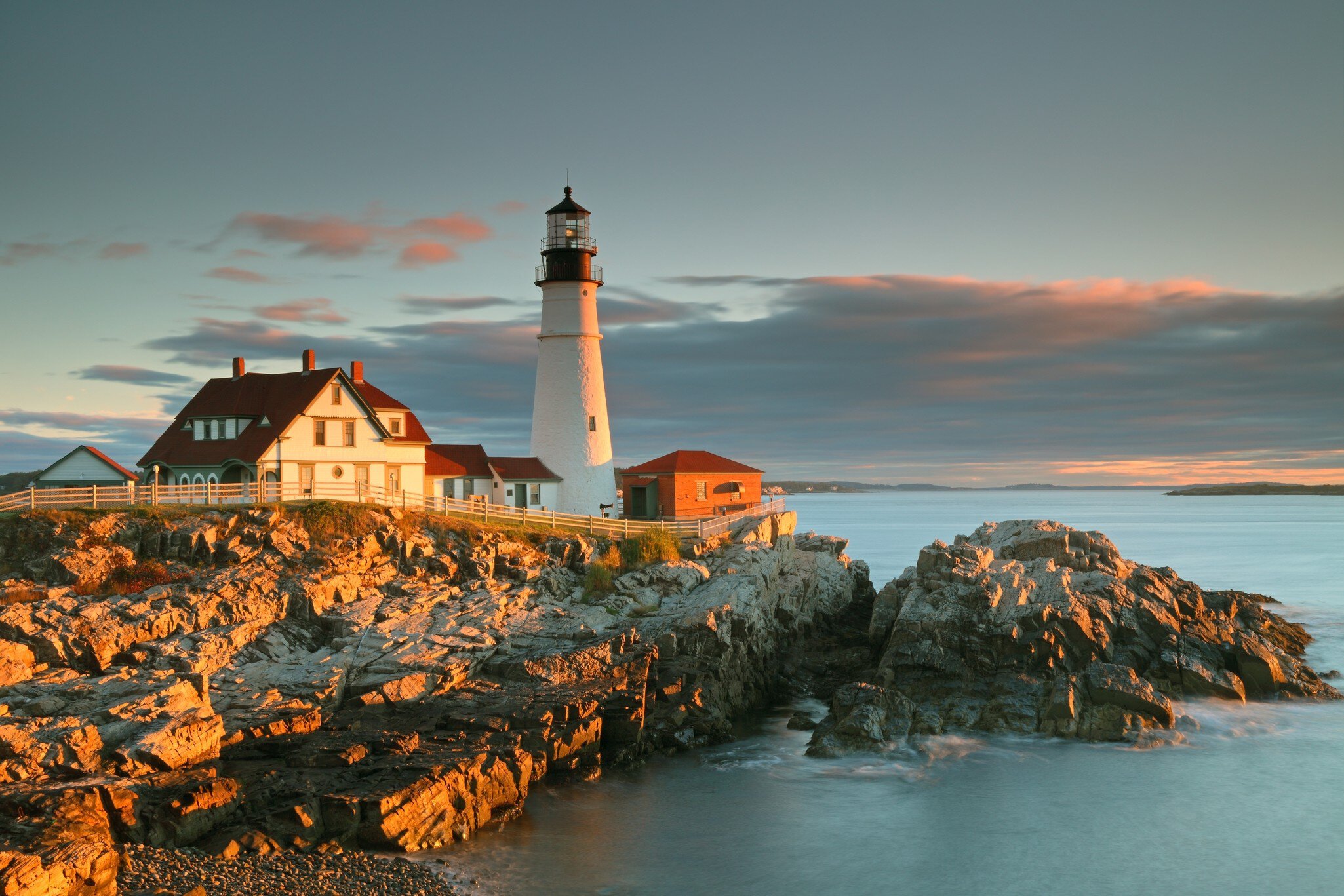 Portland Head Light and keeper's house on golden coastal rocks near Portland, Maine, at sunrise