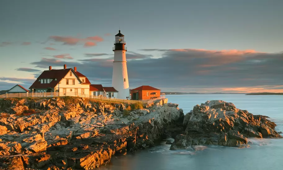 Portland Head Light and keeper's house on golden coastal rocks near Portland, Maine, at sunrise