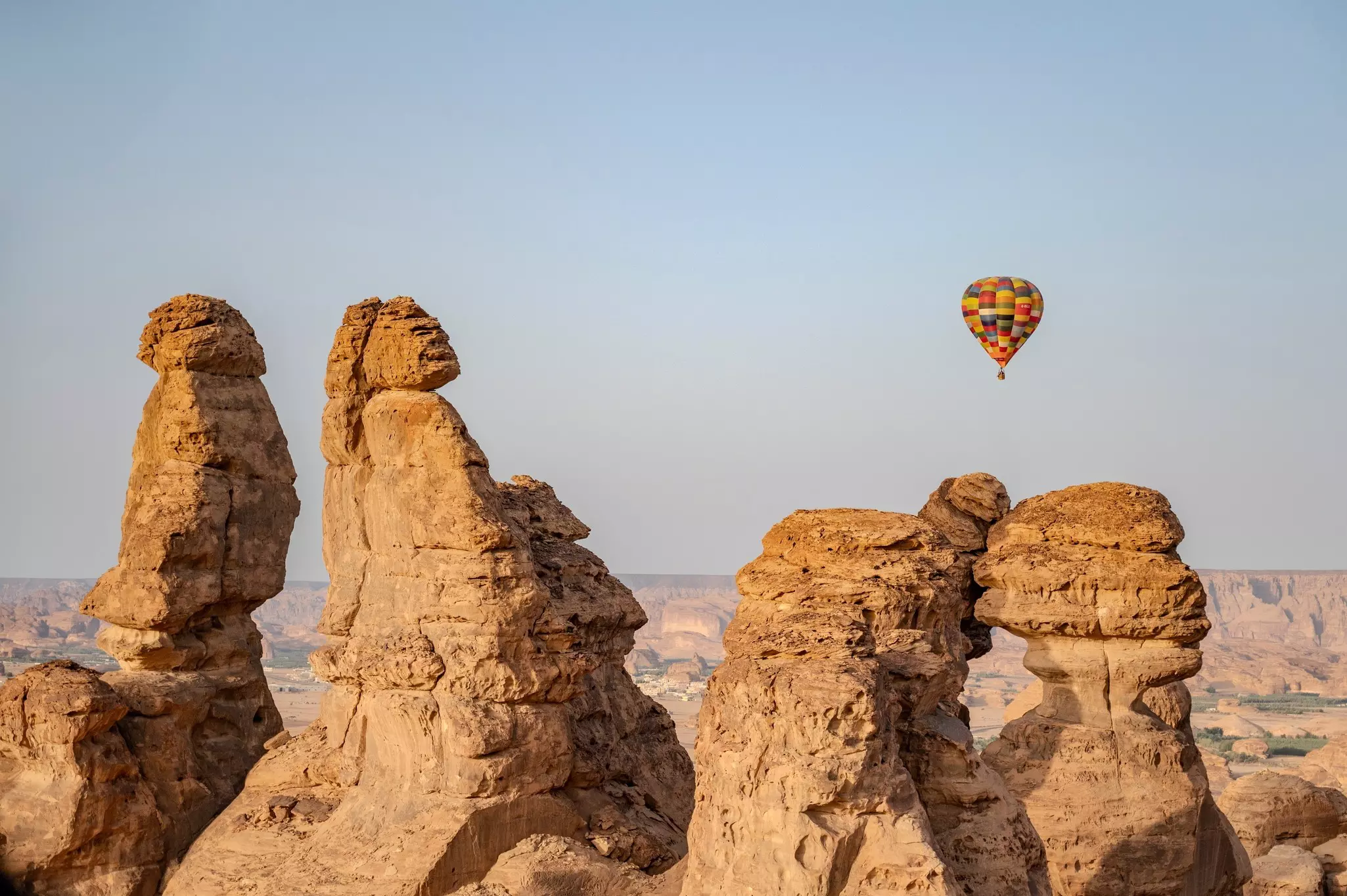 A multicolored hot-air balloon flies over over rock formations in a desert.