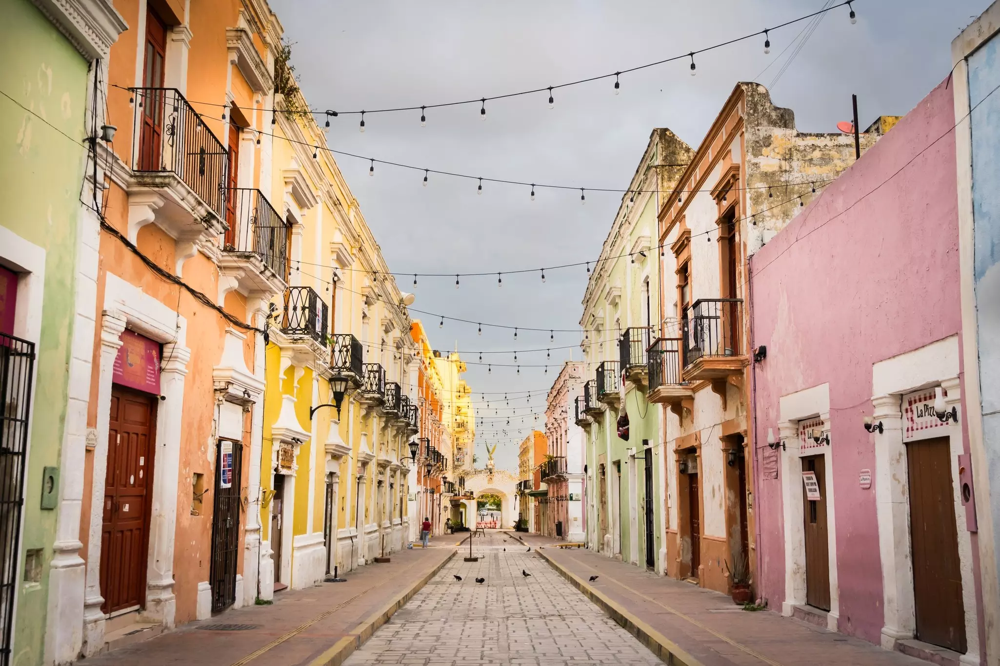 A narrow, cobbled, empty street lined with historic pastel-painted buildings is seen at dawn.