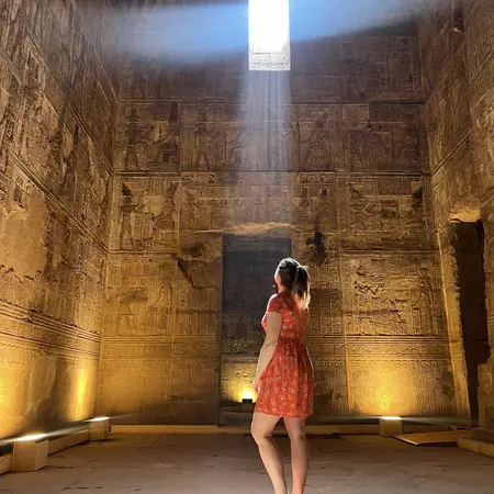 A woman in a stone room looks through a square hole of light