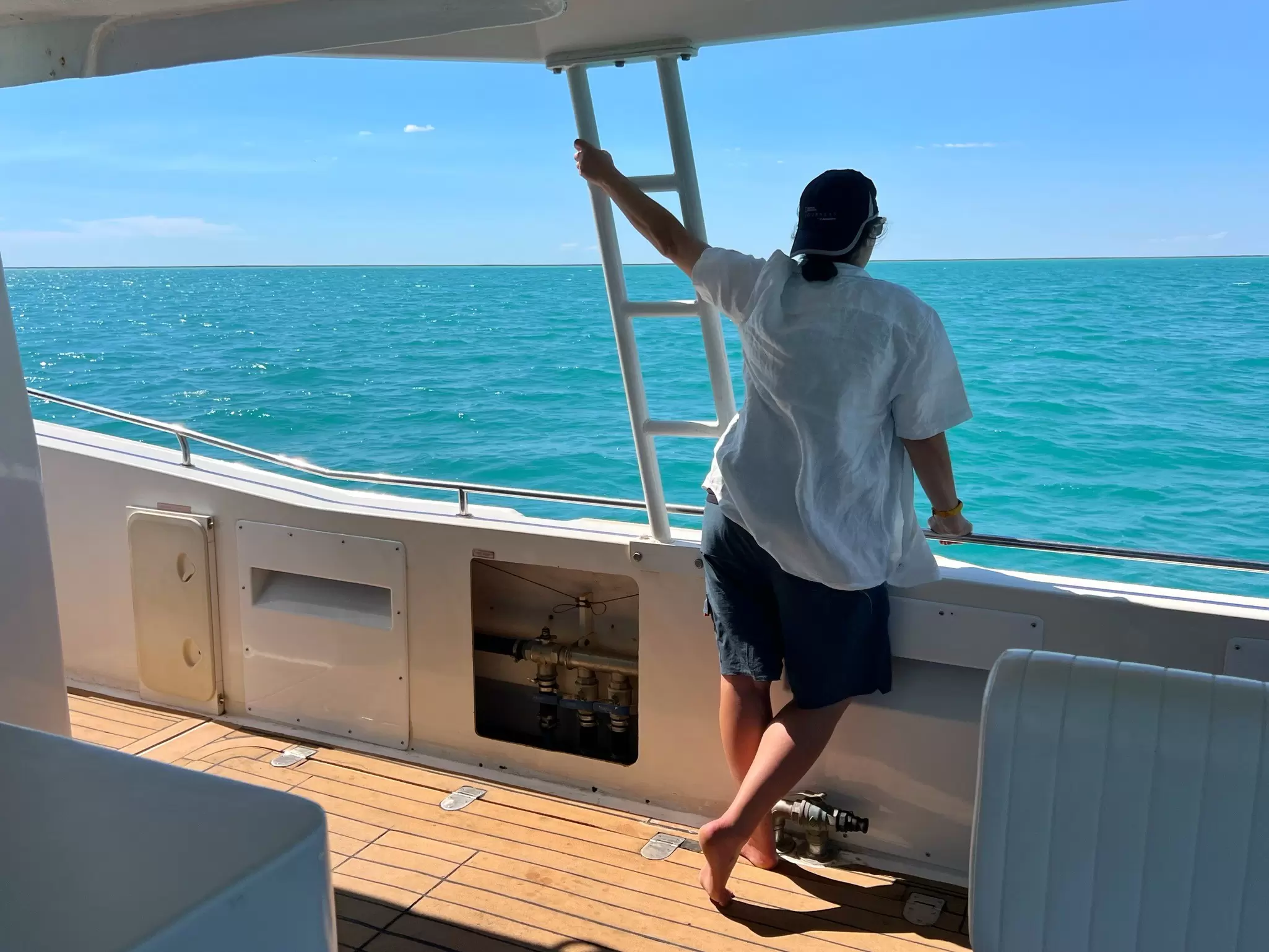 A woman in a white shirt stands on a boat looking out at ocean waters.