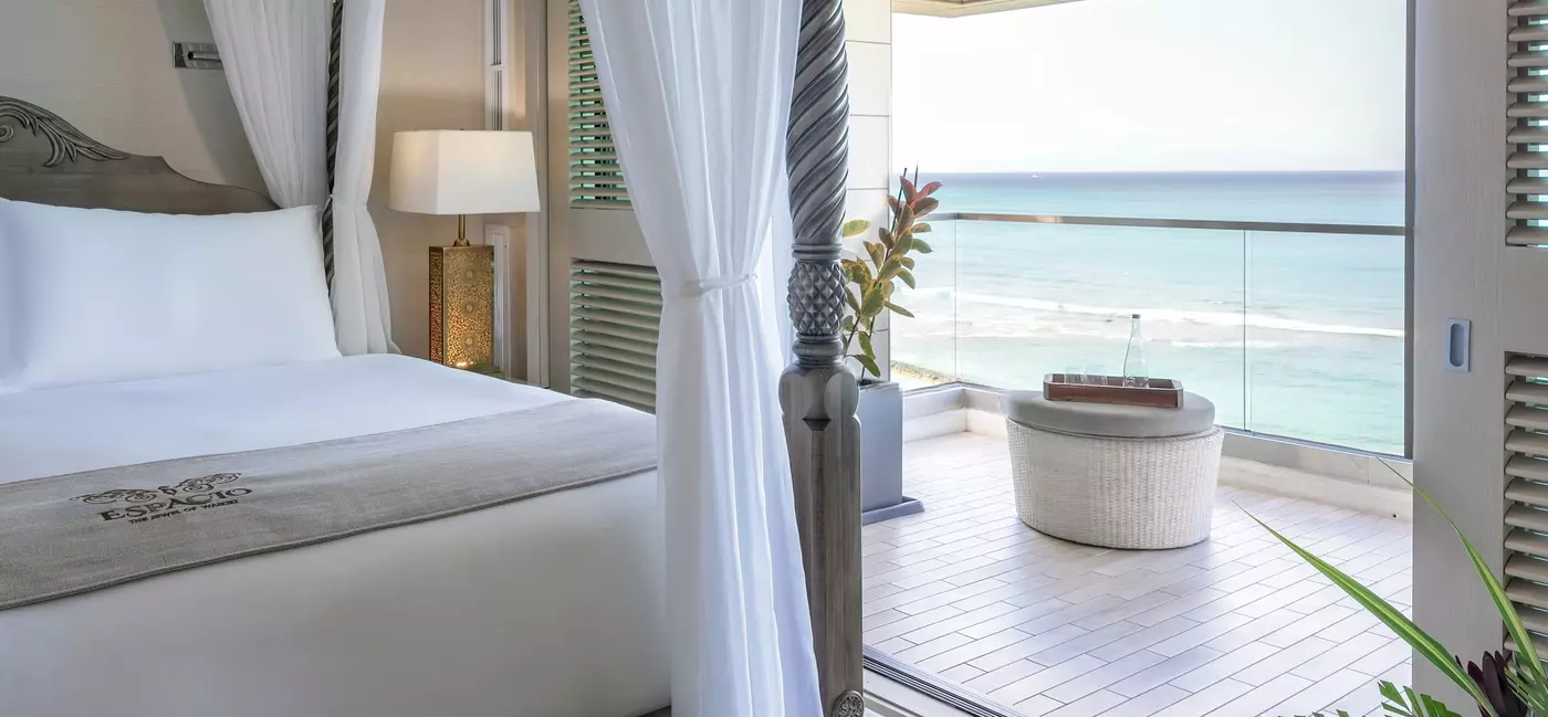 A large bed in a hotel room with views of the ocean from the balcony