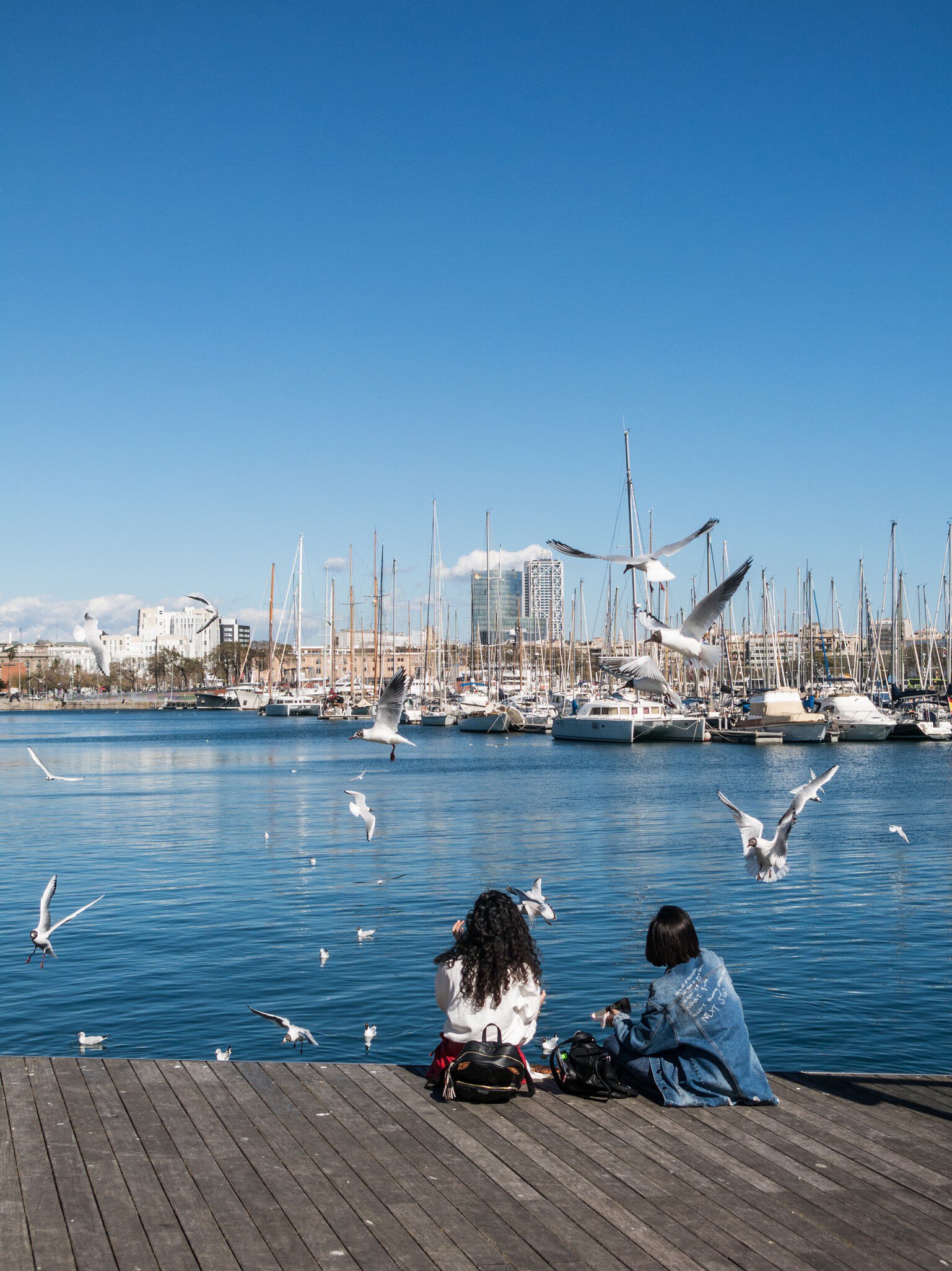 Two women sit by the water at the old port of the city of Barcelona, Spain.