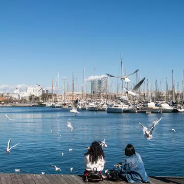 Two women sit by the water at the old port of the city of Barcelona, Spain.