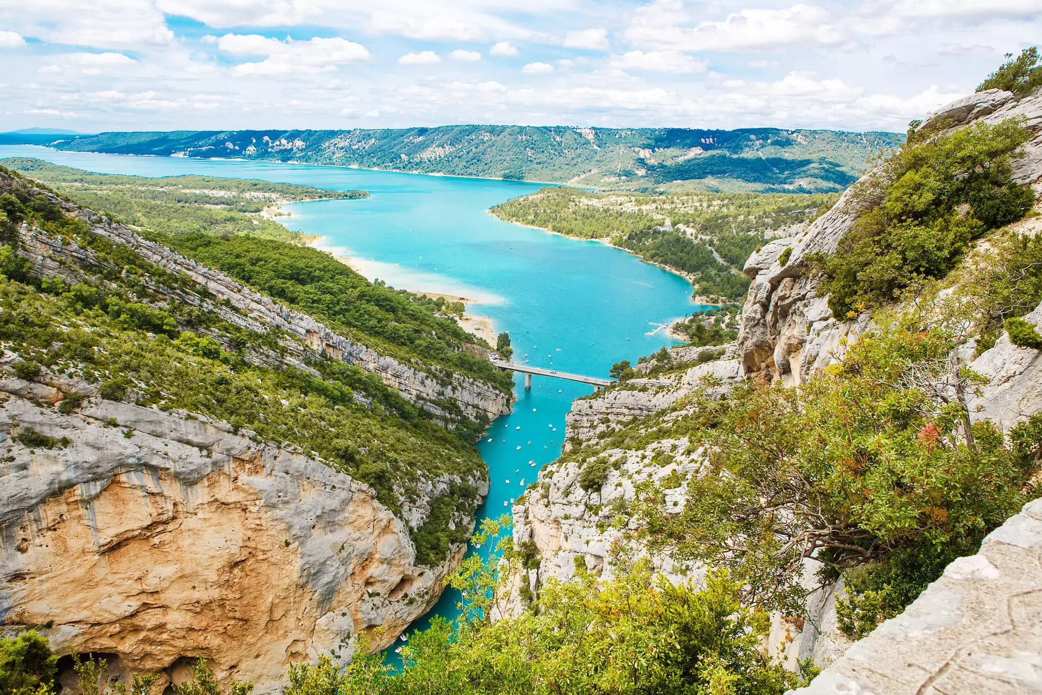 High-angle view of a gorge opening up into a lake with a road bridge