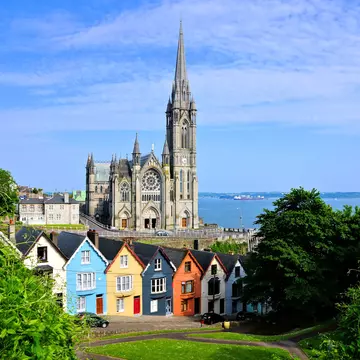 Colorful row houses with a towering cathedral in the background in the port town of Cobh, County Cork, Ireland. 