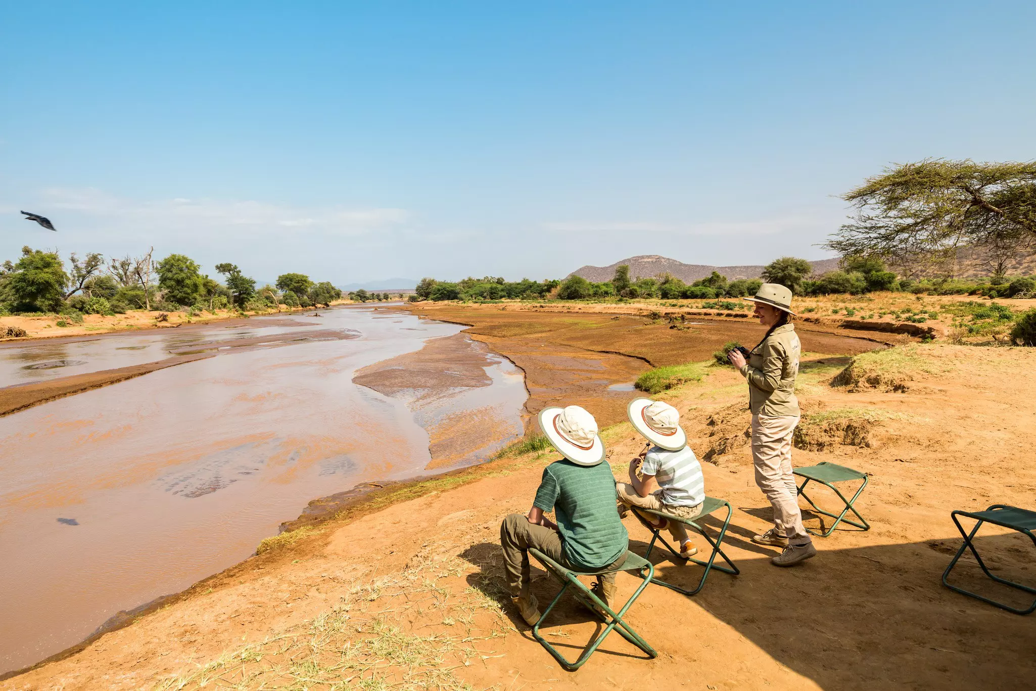 Family of mother and kids on African safari vacation enjoying Ewaso Nyiro River views in Samburu Kenya.