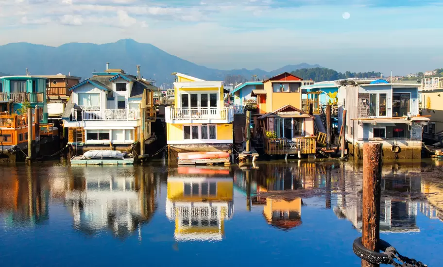 Colourful floating homes reflected in calm water at Sausalito, California, with Mount Tamalpais behind and moon above