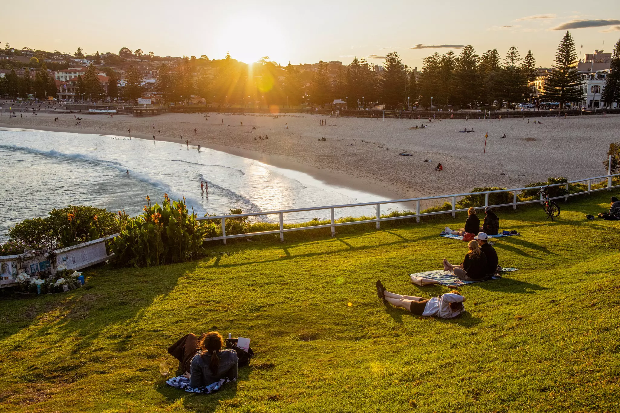 People lie on a grassy area above a sandy beach watching the sunset.