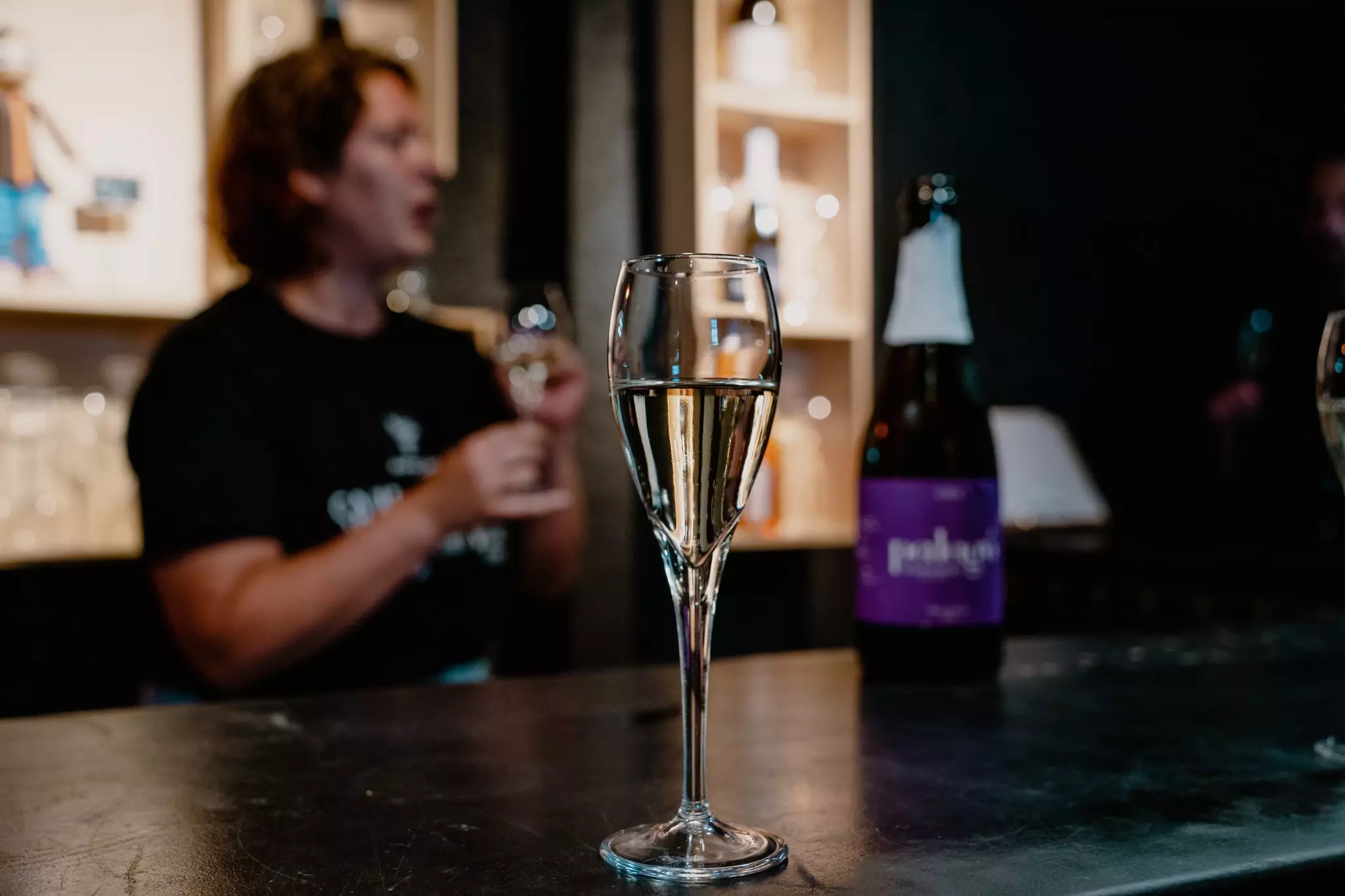 A glass of cava from the Penedès Wine Country on a bar with a server behind out of focus.